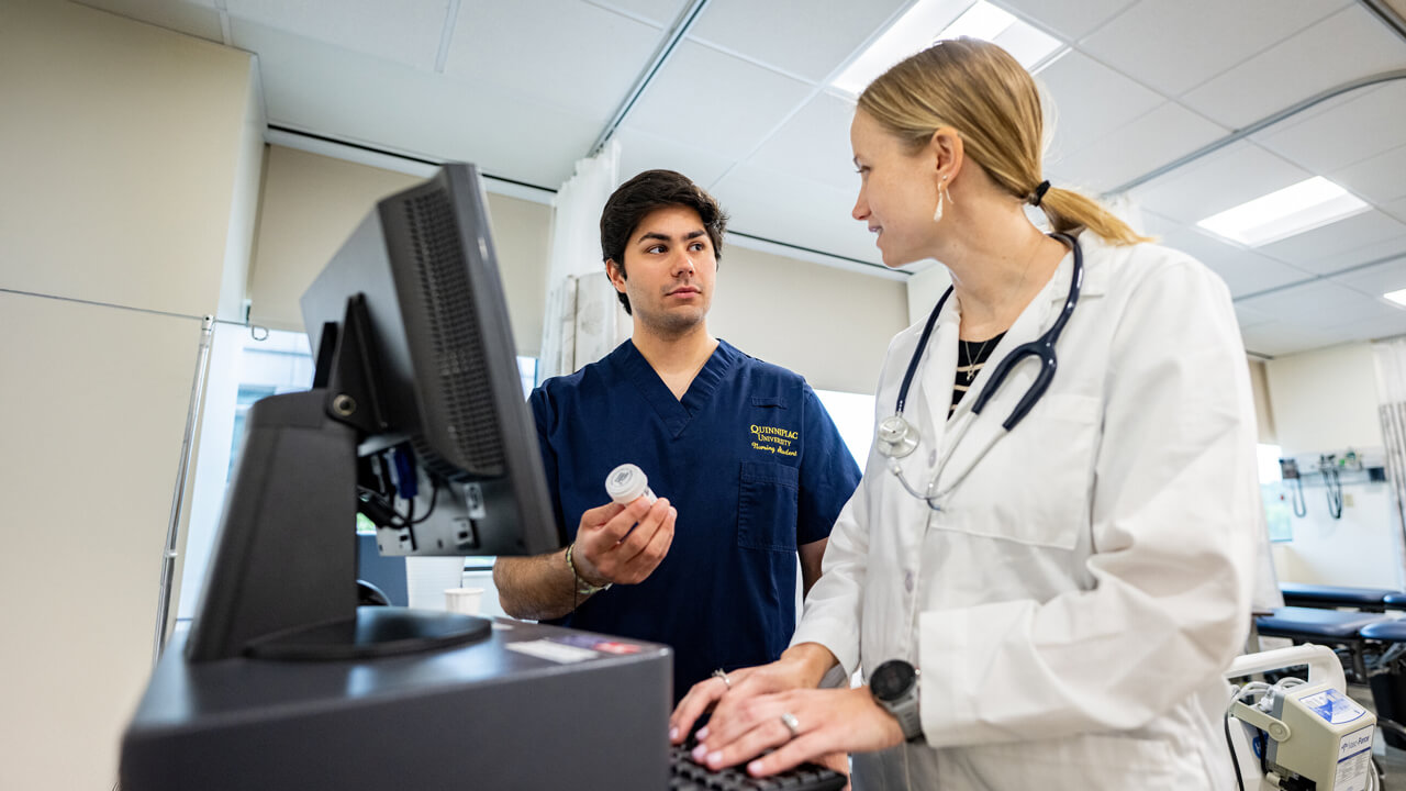 A male student looking at a female nursing instructor while holding a medication bottle