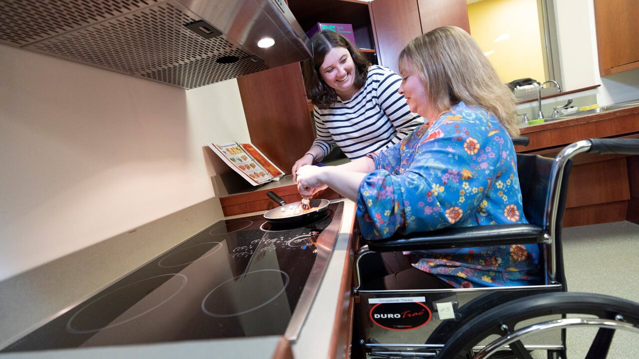 An occupational therapy student assists a handicapped person in a kitchen environment.
