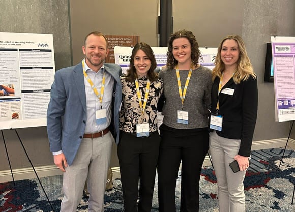 Physician assistant students pose for a photo in front of their research posters.