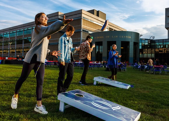 2 teams of grad students playing cornhole, one in the midst of throwing a bean bag