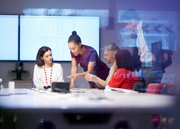 5 people talk and collaborate around laptops behind a glass wall